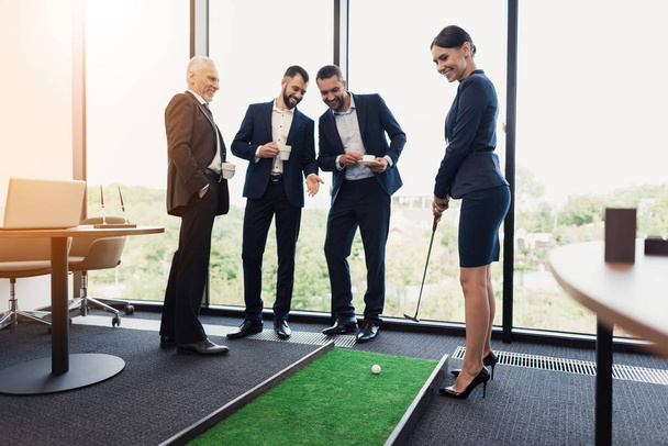 Three businessmen and business ladies play golf. A woman is holding a golf stick in the dots. Men are watching - Photo, Image