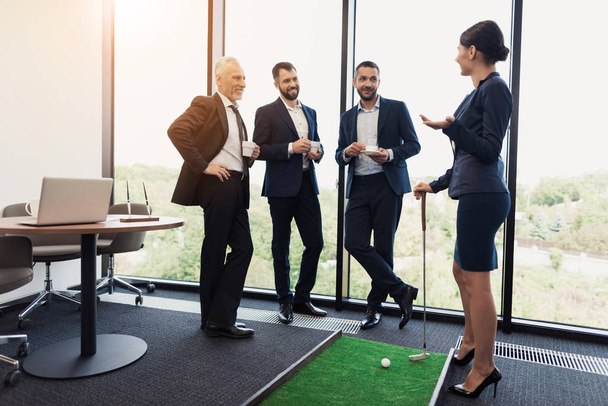 Three businessmen and business ladies play golf. A woman is holding a golf stick in the dots. Men are watching - Fotó, kép