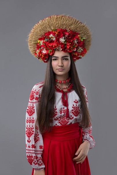 Attractive woman wears Ukrainian national dress or embroidery and wreath of flowers and spikes on a grey background - Photo, Image