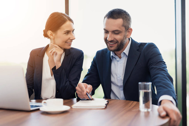 A man and a woman in strict business suits are discussing something while sitting at a table with a cup of coffee - Foto, immagini