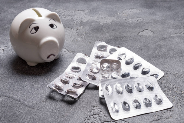 Sad piggy bank, not enough money for Medical tablet on grey background - Foto, Imagem