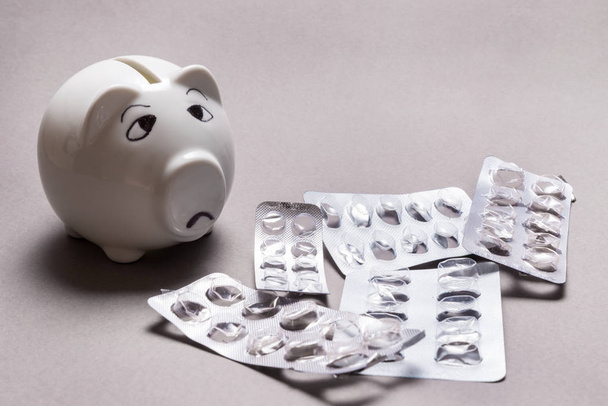Sad piggy bank, not enough money for Medical tablet on grey background - Foto, immagini