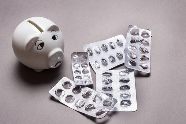 Sad piggy bank, not enough money for Medical tablet on grey background - Foto, imagen