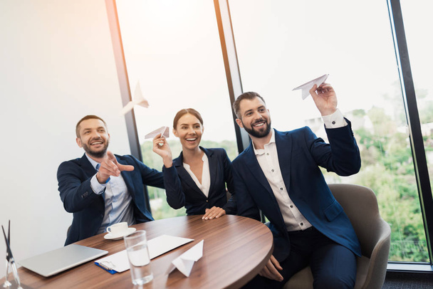 Three employees sit at the table at a meeting and are fooled. They launch paper airplanes and rejoice - Photo, image