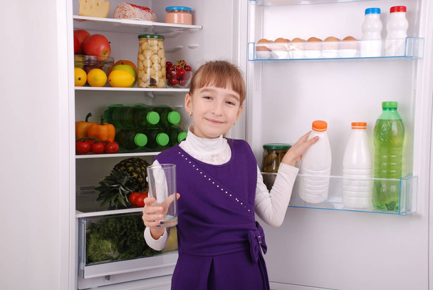Красива дівчина біля холодильника зі здоровою їжею
.  - Фото, зображення