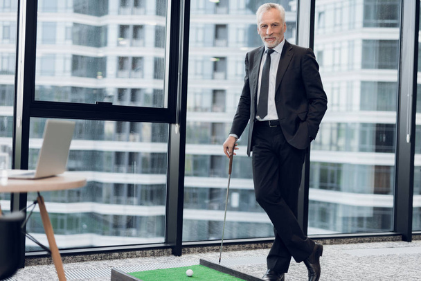 Un hombre respetable de edad avanzada en un estricto traje de negocios posando en la oficina jugando un mini juego de golf
 - Foto, imagen