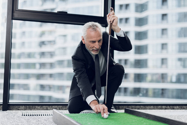 A respectable elderly man playing a mini golf in the office. He puts the ball before the blow - Фото, зображення