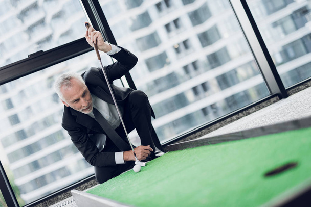 A respectable elderly man playing a mini golf in the office. He puts the ball before the blow - Фото, зображення