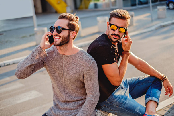 zwei Freunde, die auf der Straße sitzen und telefonieren - Foto, Bild