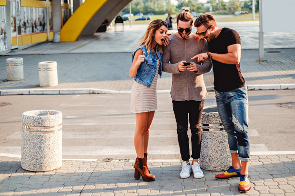 Группа людей на тротуаре смотрит на мобильный телефон
 - Фото, изображение