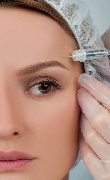 La mujer está recibiendo la inyección sobre la ceja. Tratamiento antienvejecimiento y lifting facial. Tratamiento cosmético y cirugía plástica
 - Foto, imagen