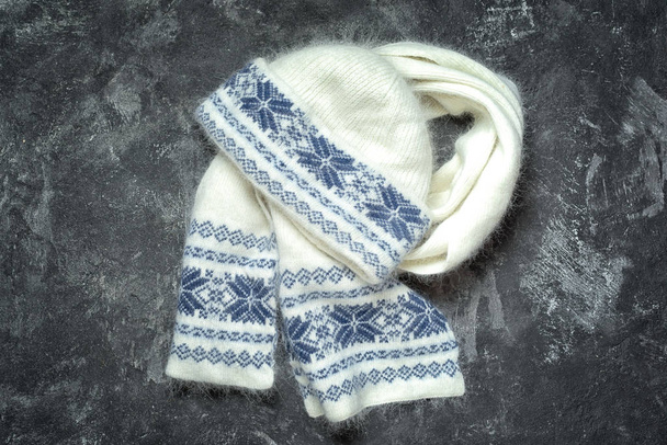 White woolen knitted hat and scarf with snowflakes pattern. Autumn and winter women's clothes. Fashion accessories. Flat lay on the dark cament background. - Photo, Image