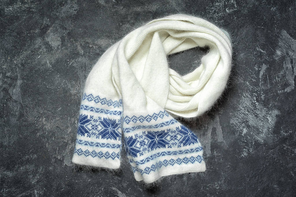White woolen knitted scarf with snowflakes pattern. Autumn and winter women's clothes. Fashion accessories. Flat lay on the dark cament background. - Photo, Image