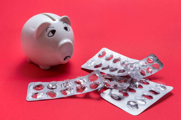 Sad piggy bank, not enough money for Medical tablet on red backg - Foto, imagen