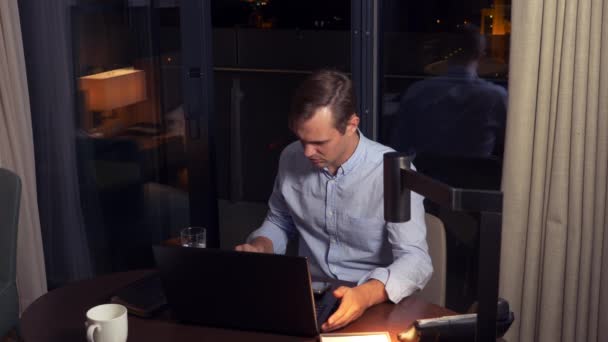 man working on a laptop at a table at night in a hotel room. 4k. - Filmagem, Vídeo