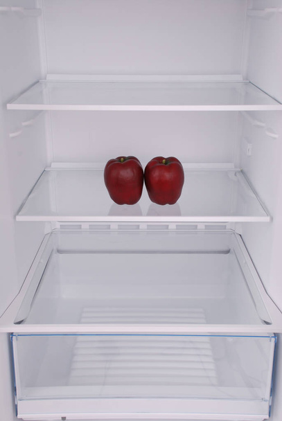 One apple in open empty refrigerator. - Фото, зображення