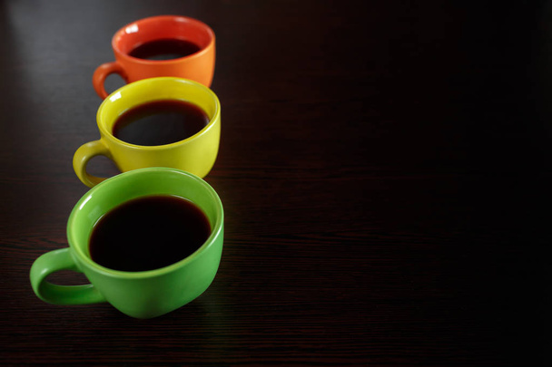 Three coffee cups stay on dark brown wooden table like lights - Photo, Image