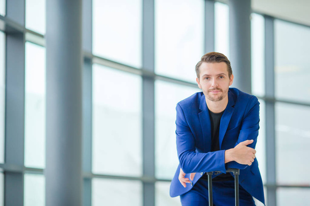 Portrait of young man in airport. Casual young boy wearing suit jacket. Caucasian man with cellphone at the airport while waiting for boarding - Fotó, kép