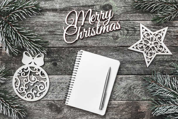 oben, oben, Blick von oben auf weiße Winterfiguren, immergrüner Zweig, Notizblock, Kugelschreiber und frohe Weihnacht auf grauem Hintergrund, mit Platz für Schrift, Grußwort. - Foto, Bild