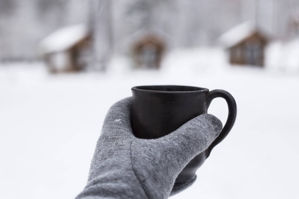 Kobiece ręce w rękawicach trzyma filiżankę kawy w śnieżnym lesie - Zdjęcie, obraz