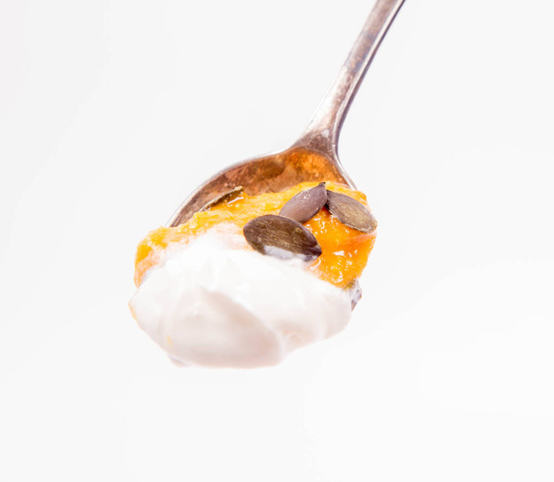 白い背景にスプーンでクリームとカボチャの種子で飾られたカボチャとニンジンのスープ - 写真・画像