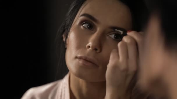Beautiful woman painting eyebrows with mascara at mirror - Felvétel, videó