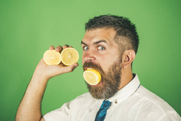 man with long beard eat lemon fruit on green background - Foto, afbeelding