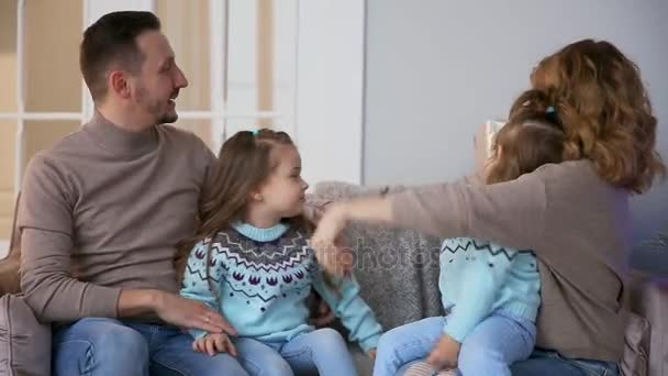 Happy family at Christmas, mum, dad and two little girls sitting at home on the sofa near the Christmas tree to open the gifts. - Filmagem, Vídeo
