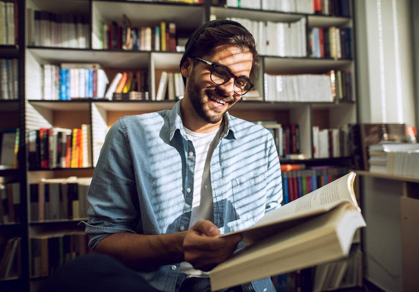portret młodych uśmiechający się student czytania książki w bibliotece - Zdjęcie, obraz