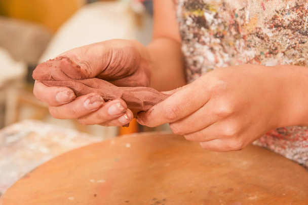 Closeup of woman ceramist hands working on sculpture on wooden table in workshop - Фото, изображение