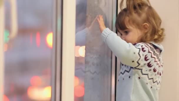 Dziewczynka stoi na parapecie w zimie i wygląda przez okno o przejeżdżających samochodów. - Materiał filmowy, wideo