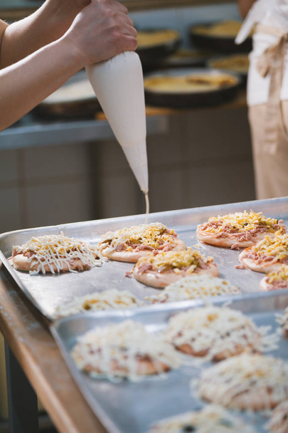 Повар кладет соус на мини-пиццу в пекарню
 - Фото, изображение