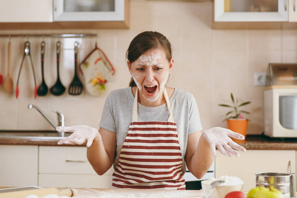 A young perplexed and confused woman sitting at a table with flour and going to prepare a Christmas cakes in the kitchen. Cooking home. Prepare food. - Photo, Image