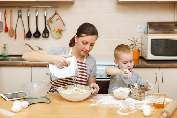 Маленький мальчик помогает маме готовить рождественское имбирное печенье на светлой кухне с табличкой на столе. Счастливая семейная мама 30-35 лет и ребенок 2-3 в выходные утром дома. Концепция отношений
 - Фото, изображение