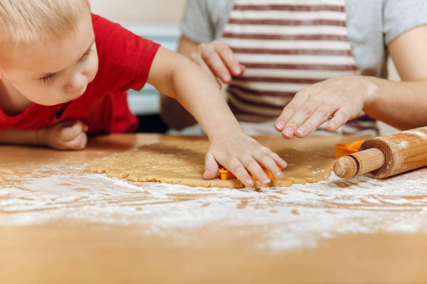 子供の小さな男の子の母親の料理クリスマス明るいキッチンでジンジャー ビスケットに役立ちます。幸せ家族ママ 30-35 歳と子でクッキーを 2-3 ロール生地を切り取って家します。関係との愛の概念 - 写真・画像