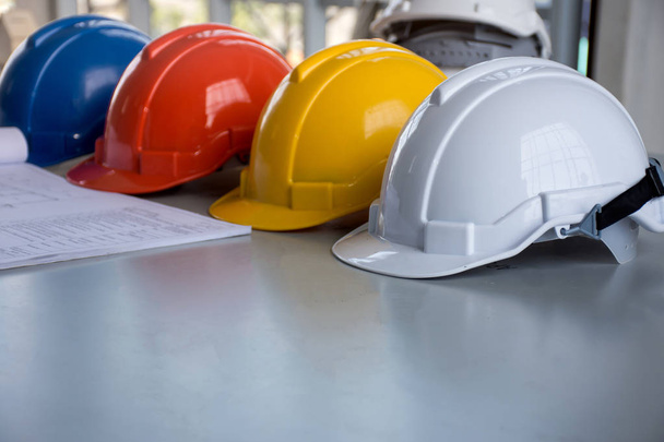 Kavramın mimarı, mühendisi ya da işçi daralma ekipman/Emanet işbirliği çalışmalarında güvenliği projesi için masaya Blueprint ve beyaz, mavi, kırmızı ve sarı zor emanet kask şapka - Fotoğraf, Görsel