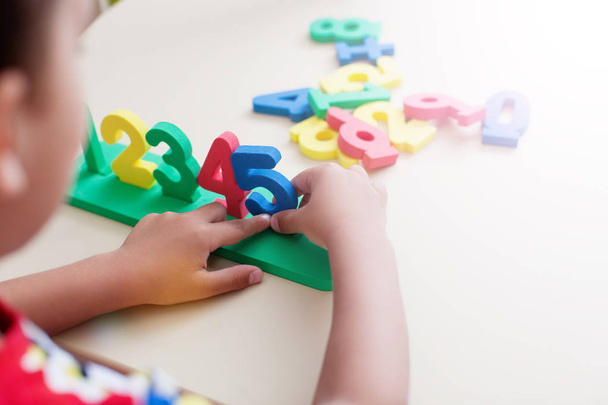 Gros plan de mains d'enfant garçon jouant avec des nombres colorés sur fond de table blanche
 - Photo, image