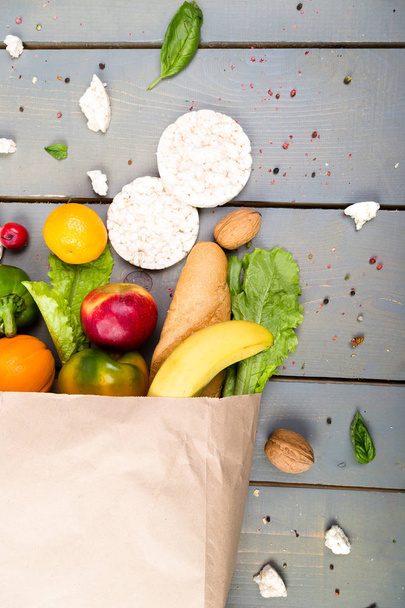 Grocery shopping concept. Different food in paper bag on wooden background.  Flat lay. - Photo, Image