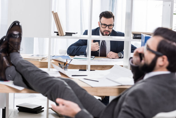 businessman trying to work when colleague talking by smartphone with legs on table  - Foto, Imagem