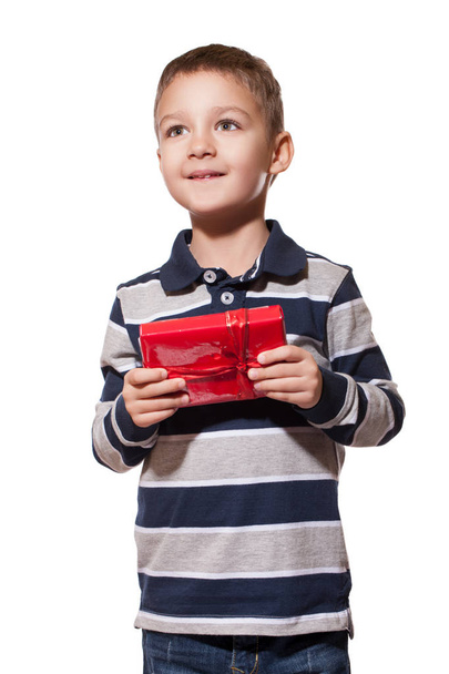 Studio shot of cute little boy wearing striped shirt standing on white studio background with red gift box in hands  - Photo, Image