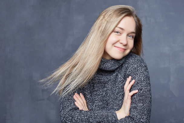 Studio shot of beautiful positive friendly-looking young Caucasian woman with lovely sincere smile feeling thankful and grateful, showing heart filled with love and gratitude, wearing warm sweater. - Photo, Image