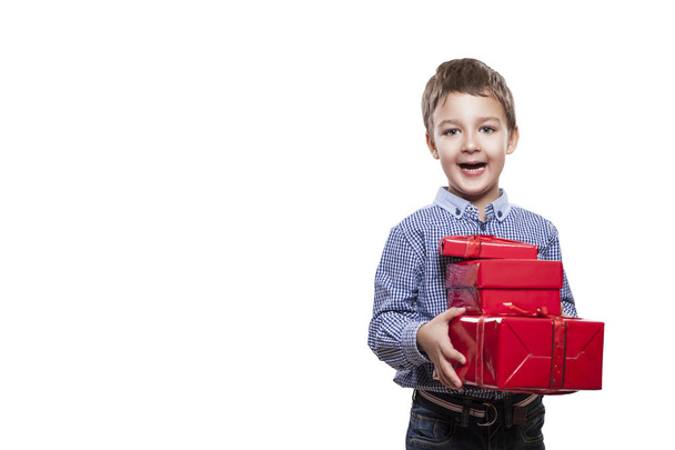 Studio shot of cute little boy wearing checkered shirt and dark jeans standing on white studio background with red gift boxes in hands  - Fotoğraf, Görsel
