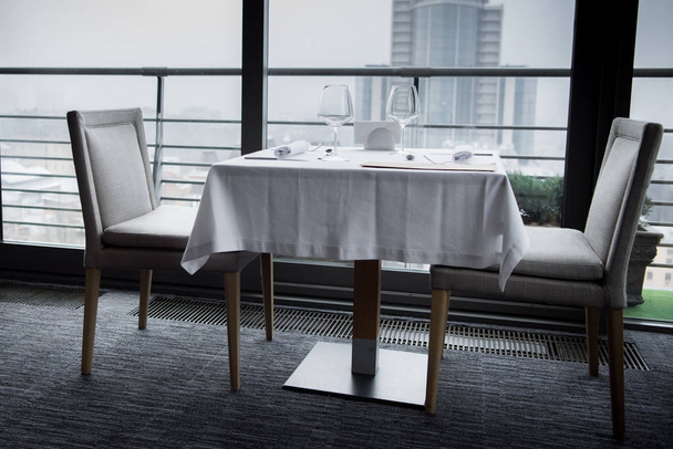 стол со столовыми приборами, пустыми бокалами и меню на белой скатерти в ресторане
 - Фото, изображение