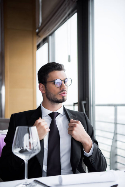 hombre pensativo en traje y anteojos mirando hacia otro lado mientras espera el pedido en el restaurante
 - Foto, Imagen