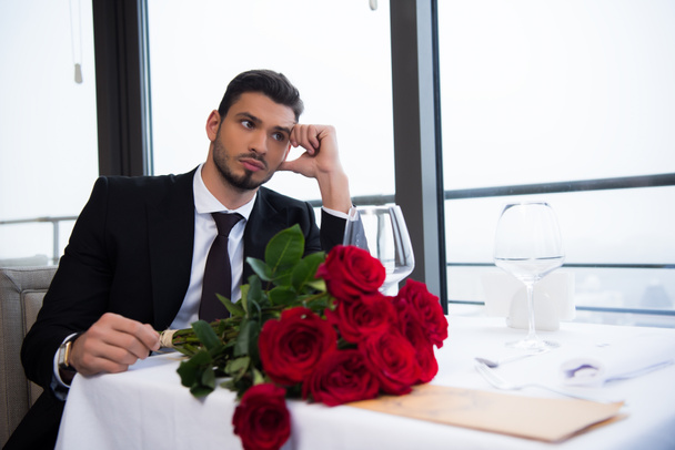 Junger Mann im Anzug mit Strauß roter Rosen wartet im Restaurant auf Freundin - Foto, Bild