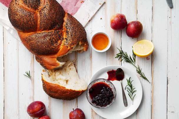 Traditional jewish bread brown challah on white wooden background with fruits and honey. Rustic concept. Copy space - Фото, изображение