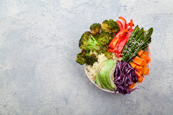 Tasty healthy bowl for lunch with couscous, baked broccoli and carrots cut in cubes, fried peas, avocados and red cabbage. Easy vegetarian diet concept. Rustic background, space for text. - Foto, imagen