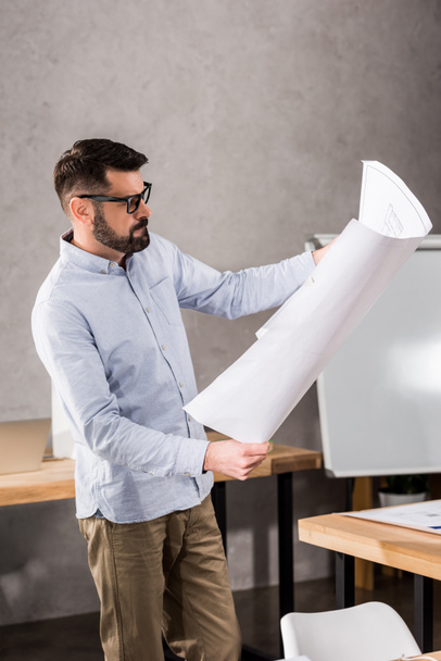 handsome architect looking at blueprint in office - Foto, afbeelding