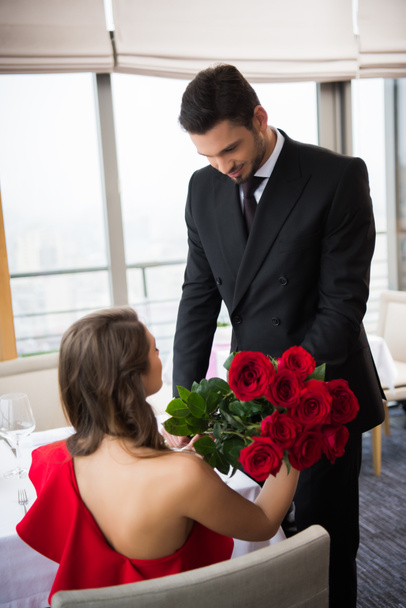 Teilbild eines Mannes, der Freundin am Valentinstag in Restaurant einen Rosenstrauß überreicht - Foto, Bild