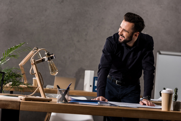 smiling architect leaning on working table and looking away - Photo, Image